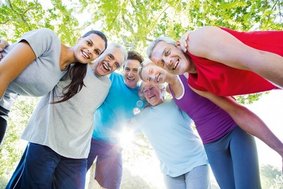 Sechs Menschen in Sportkleidung stehen unter einem Baum im Kreis und haben sich die Arme um die Schultern gelegt.